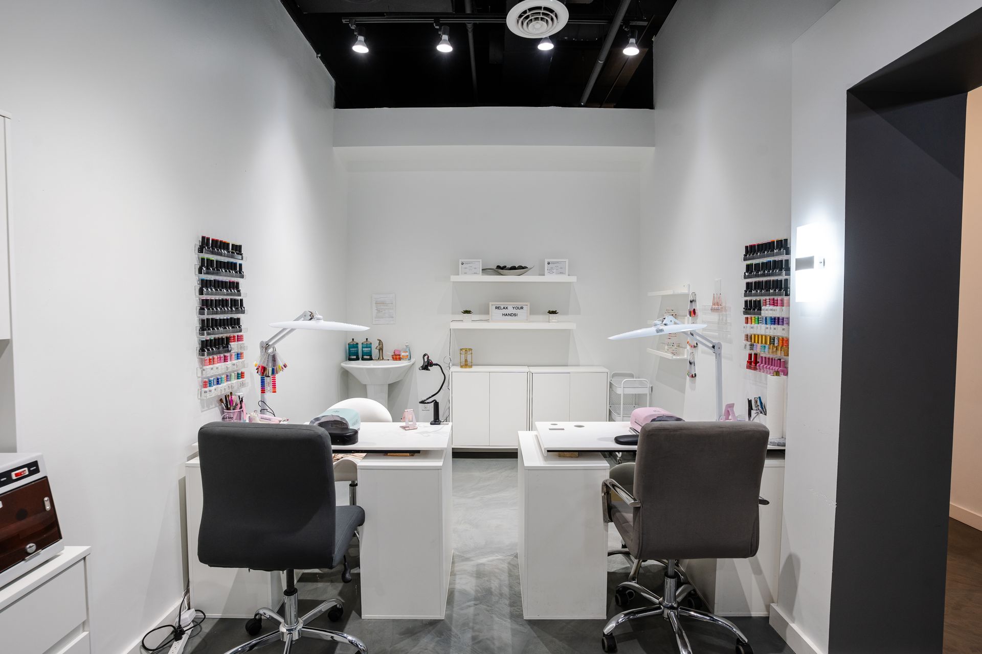 Nail salon interior with two manicure stations, white walls, and displays of nail polish colors.