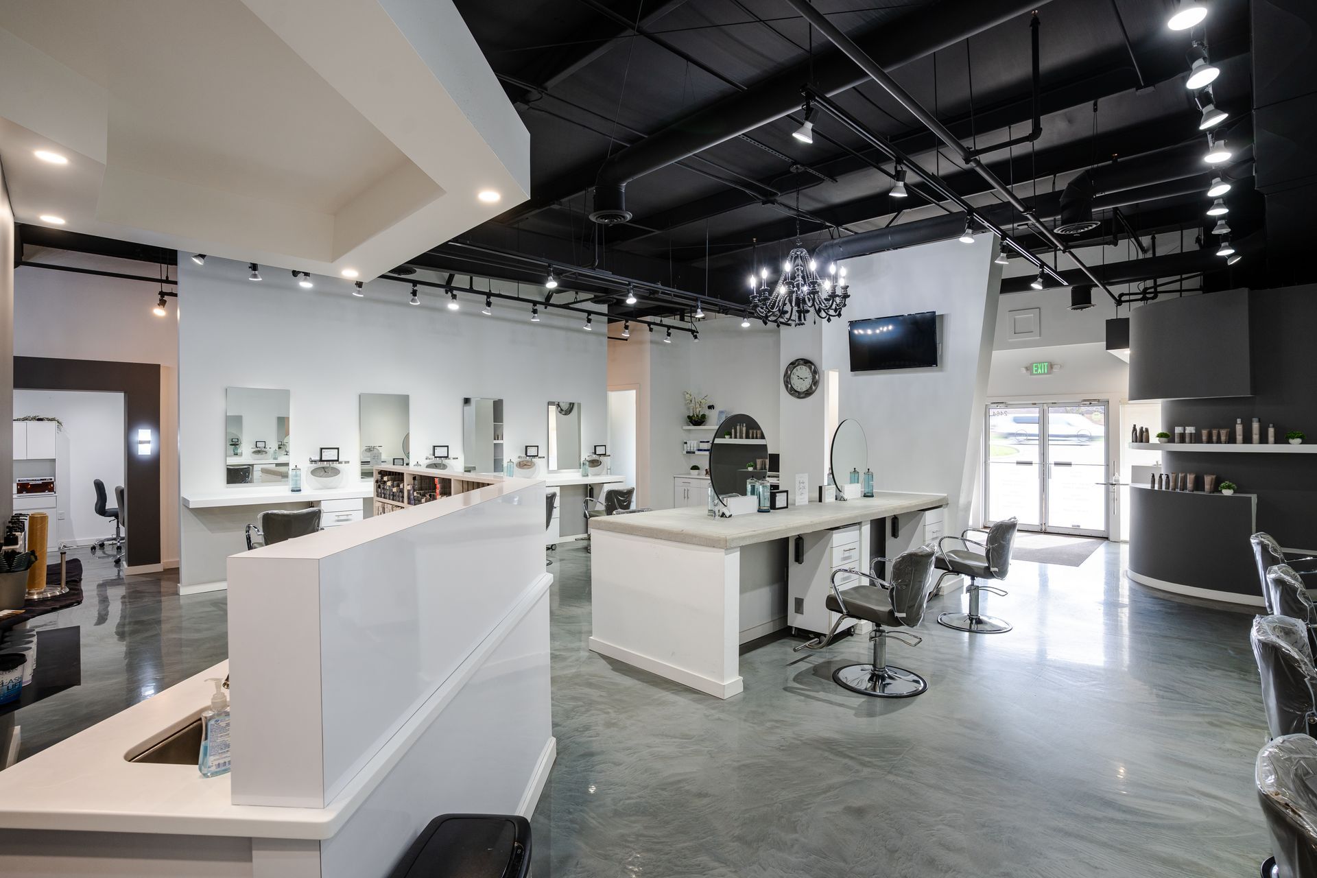 Hair salon interior with white and gray decor; hair stations, counter, and a waiting area.