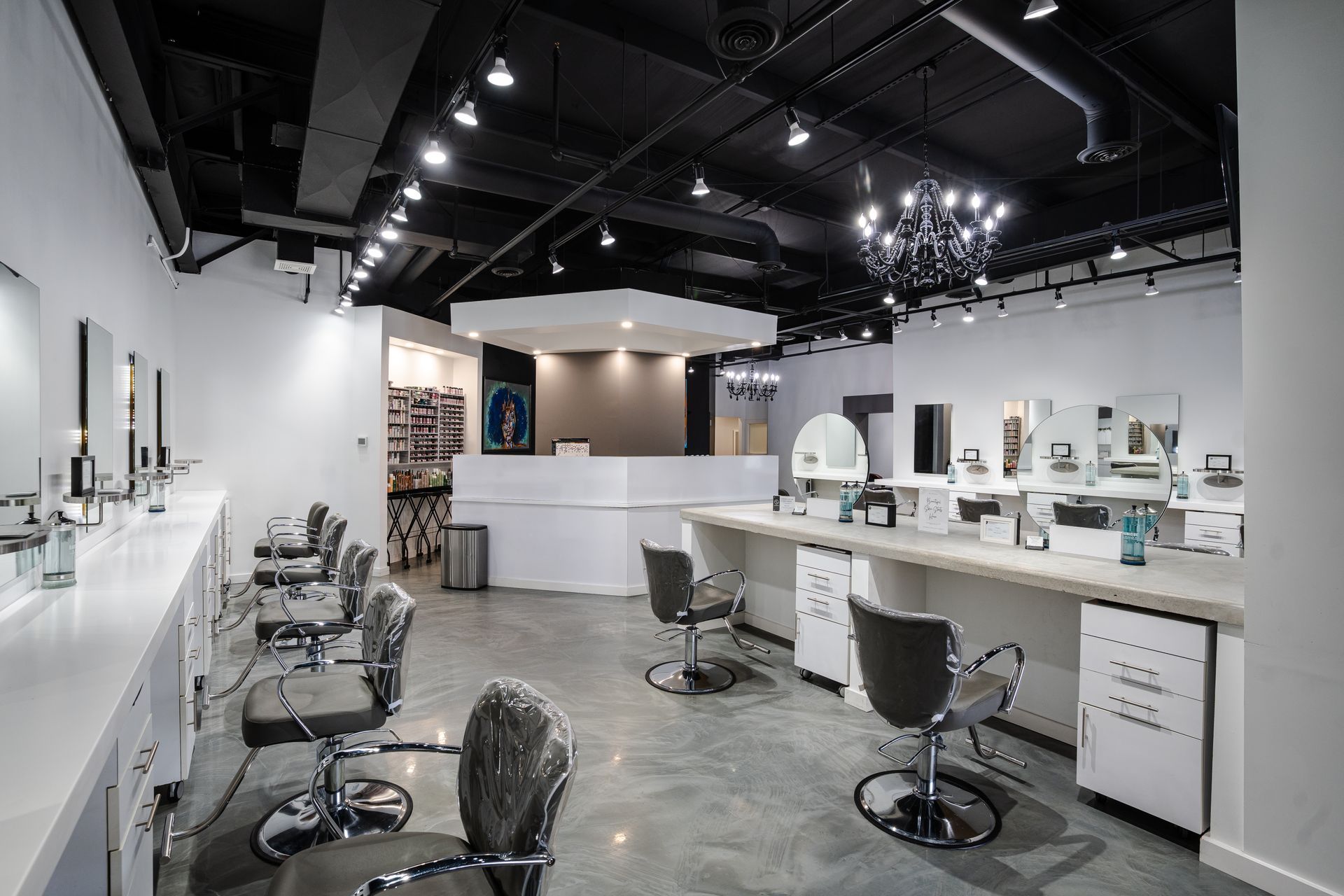 Hair salon interior with styling stations, chairs, and a front desk. White and gray tones, black ceiling.
