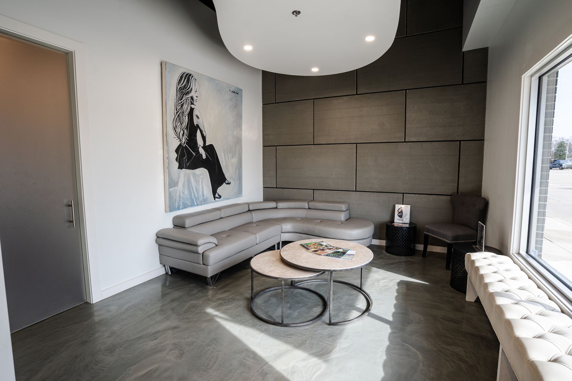 Modern waiting room with gray curved sofa, art, and coffee tables.