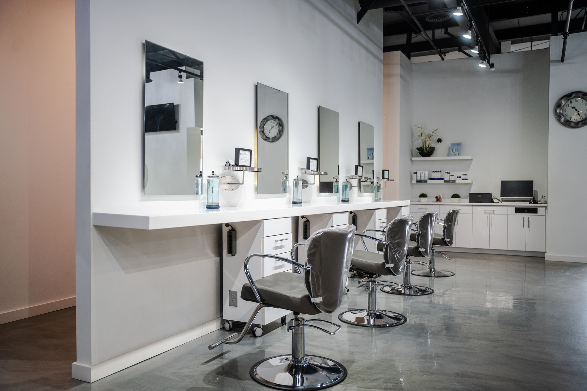Hair salon with mirrors, chairs, and styling stations along a white wall, gray floor.