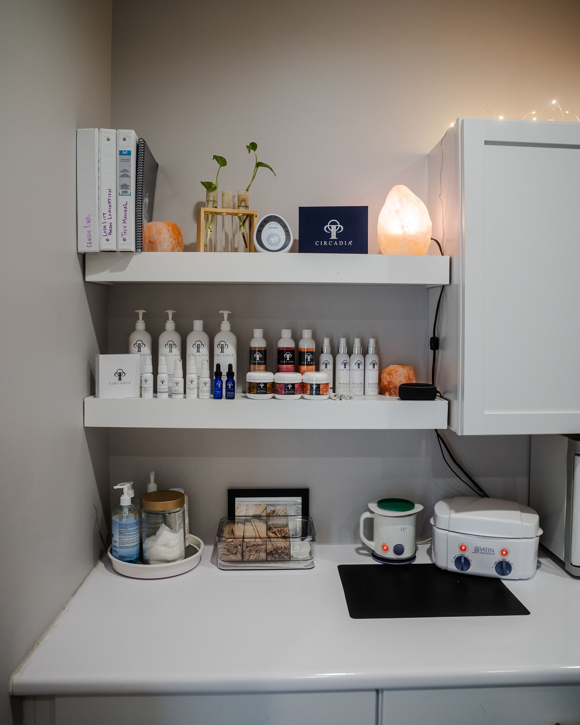 White shelves on a wall displaying self-care products, with a small desk and cabinet.