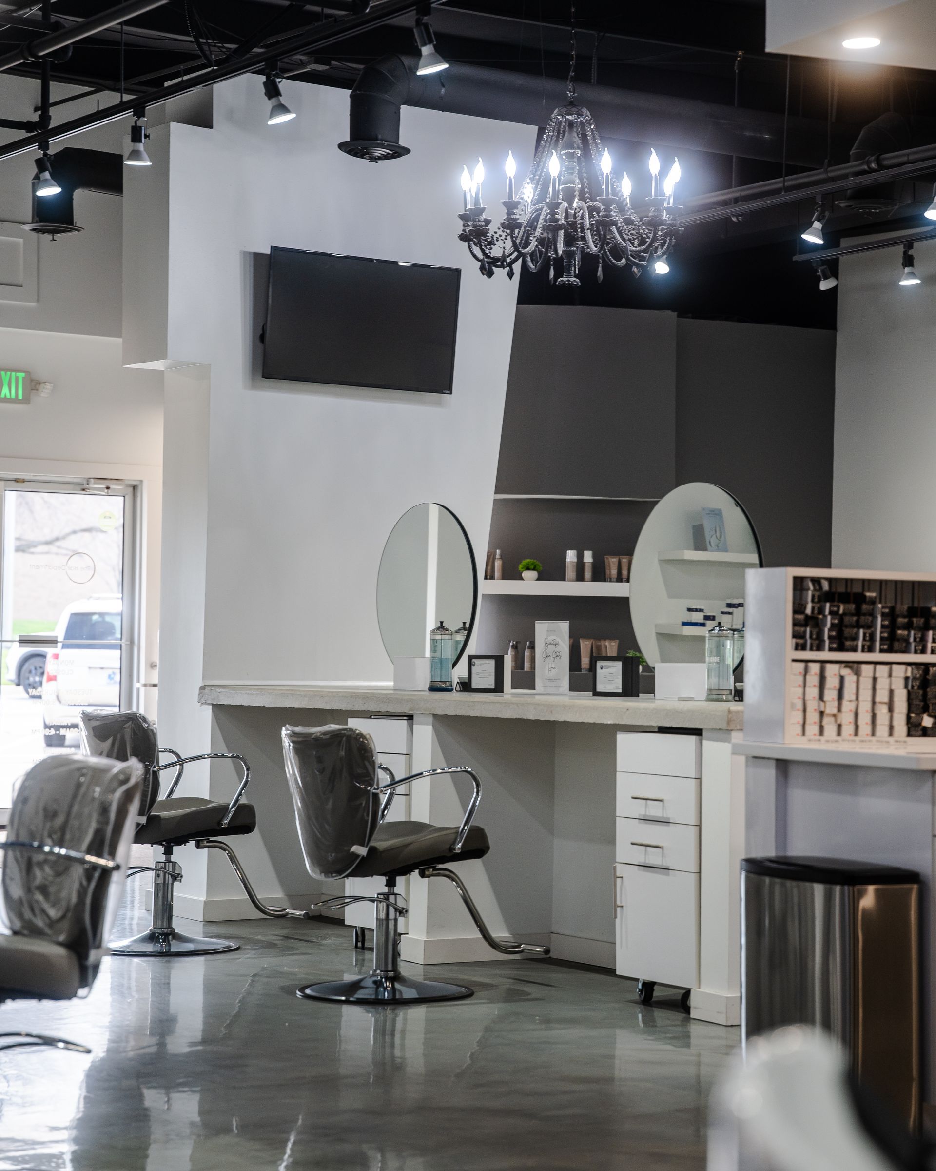 Hair salon interior with styling stations, mirrors, and a decorative chandelier.