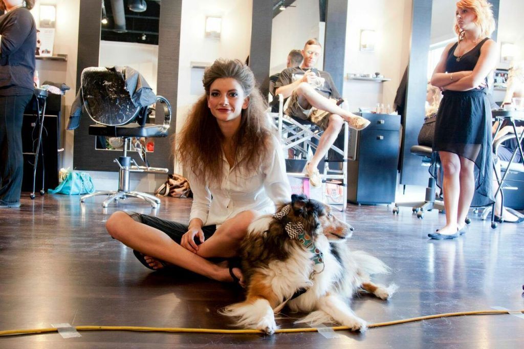 Woman sitting cross-legged with a dog in a salon. Other people and equipment are in the background.