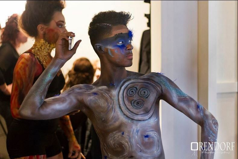 Man with body paint and blue face paint poses backstage.
