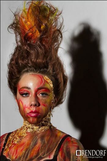 Woman with elaborate fiery makeup and hairstyle, shadow on wall.