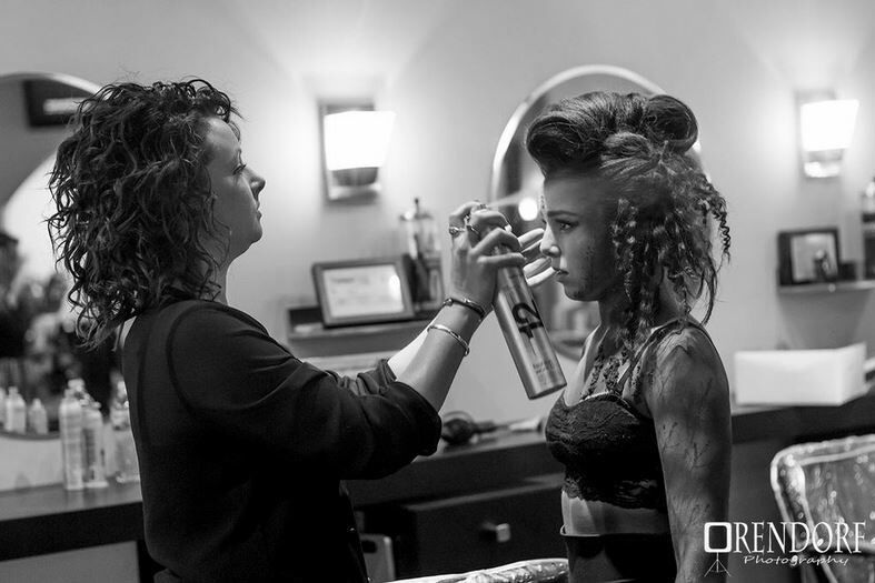Hair stylist sprays hairspray on a client with elaborately styled hair in a salon.