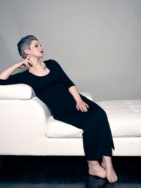 Woman in black dress reclines on white sofa, looking upward with hand on chin.