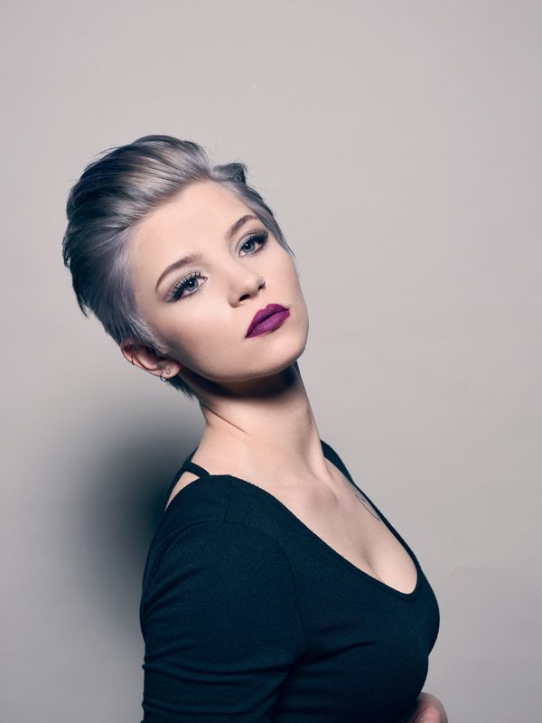 Woman with short, silver hair and dark purple lipstick, angled toward the camera, wearing a black top.