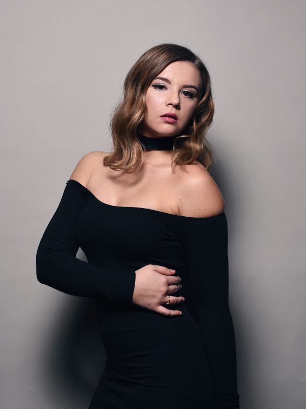 Woman in black off-the-shoulder dress and choker, posing against a gray background.
