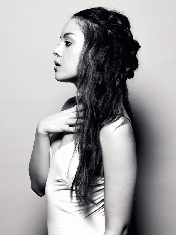Woman in side profile, wearing a cream-colored top, with a braided updo.