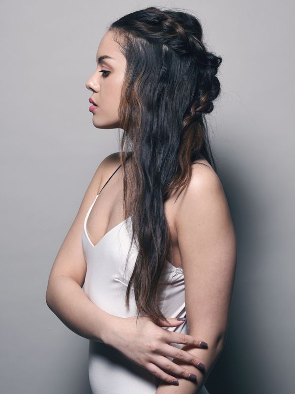 Woman with dark hair in a white dress, side profile. Braided hair detail, against a gray background.