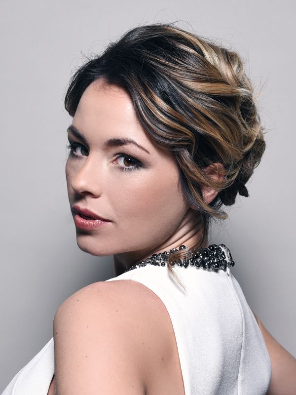 Woman with dark hair styled up, looking over her shoulder. Wearing a white dress with a beaded neckline.