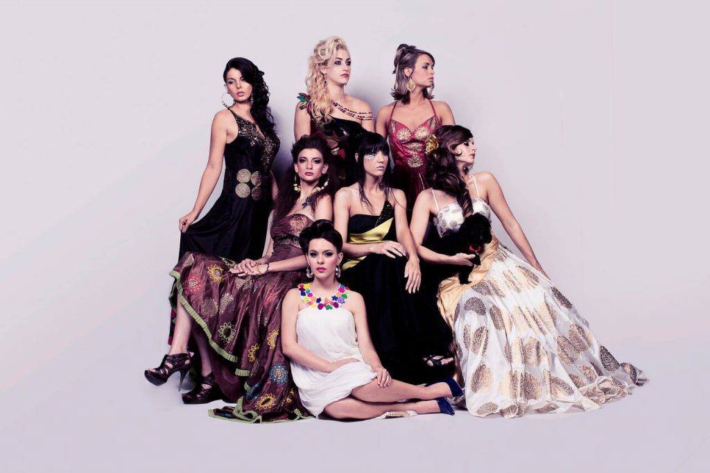 Group of women in evening gowns, posing together against a plain background.