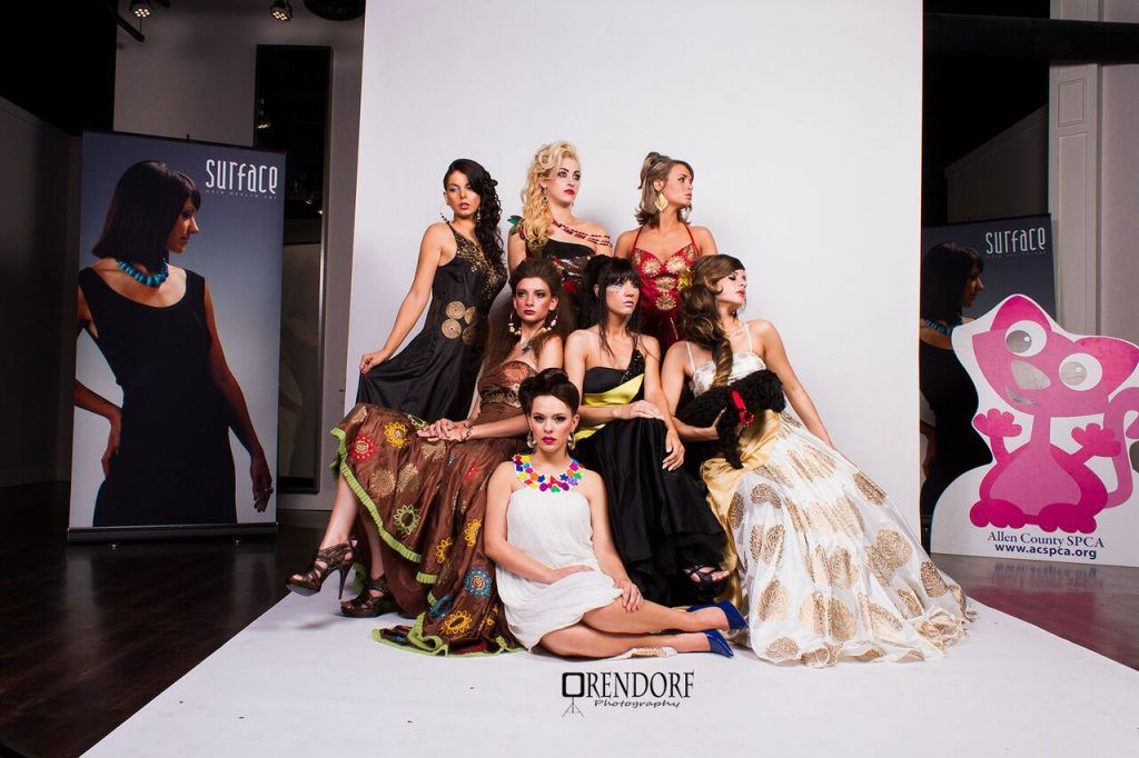 Group of women in formal dresses posing on a white runway in a studio.