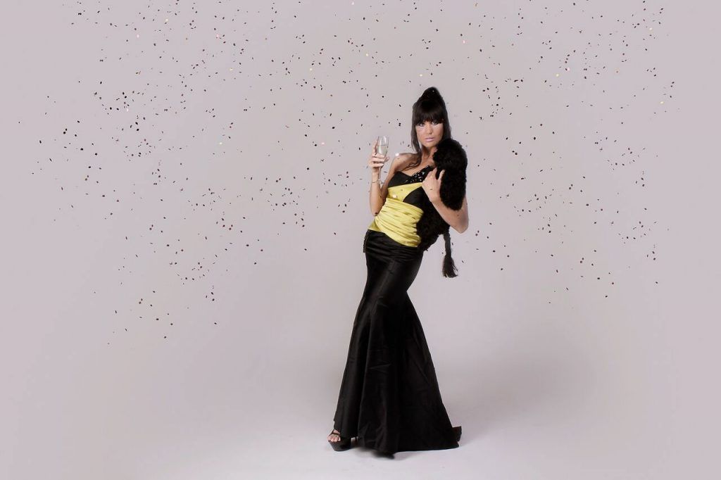 Woman in evening gown, holding champagne, confetti falling.