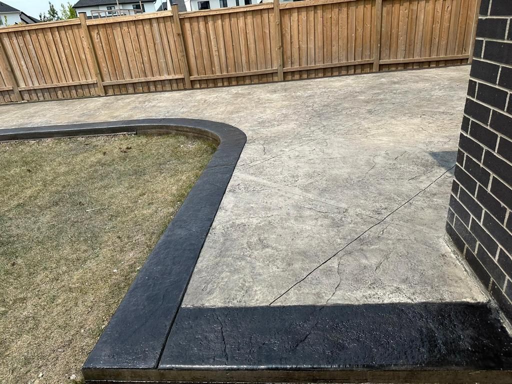 Concrete patio corner with black edging beside grass and a wooden fence