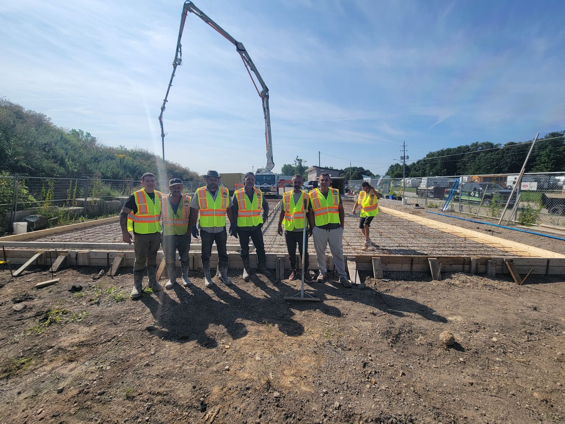 Construction crew in neon safety vests on a rebar foundation, with a concrete pump boom overhead.