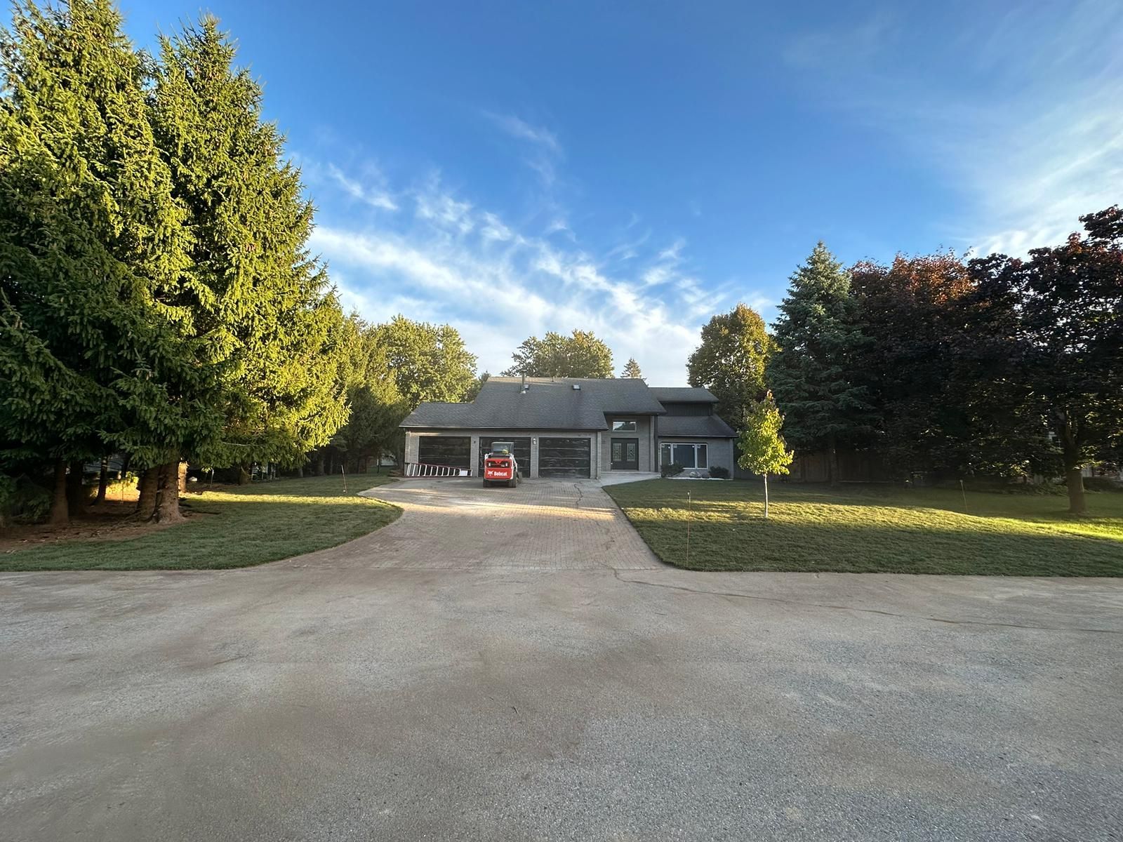 Driveway leading to a gray house with a red car, surrounded by trees and open lawn