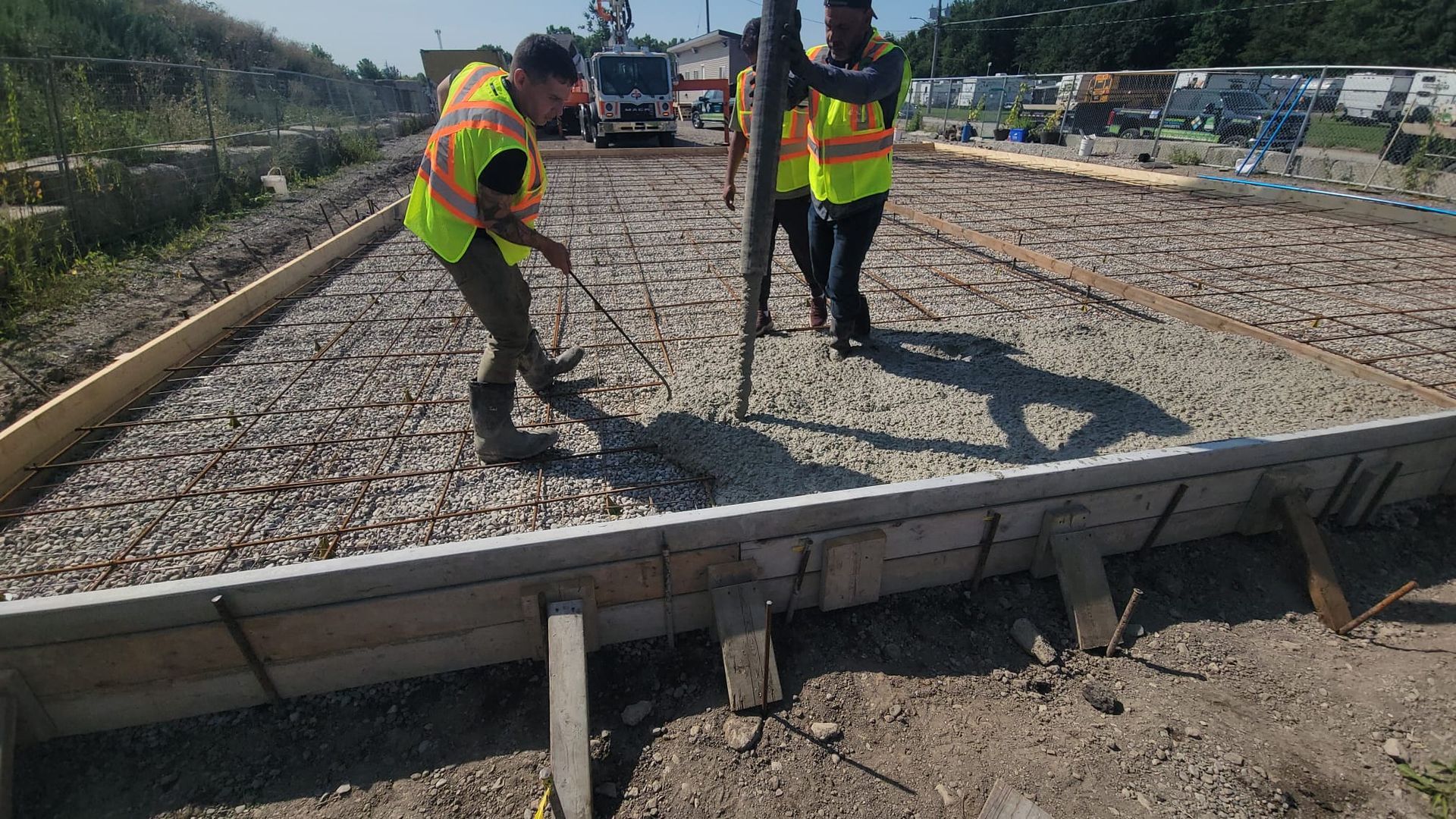 Two construction workers in neon vests leveling gravel on a railroad track under repair