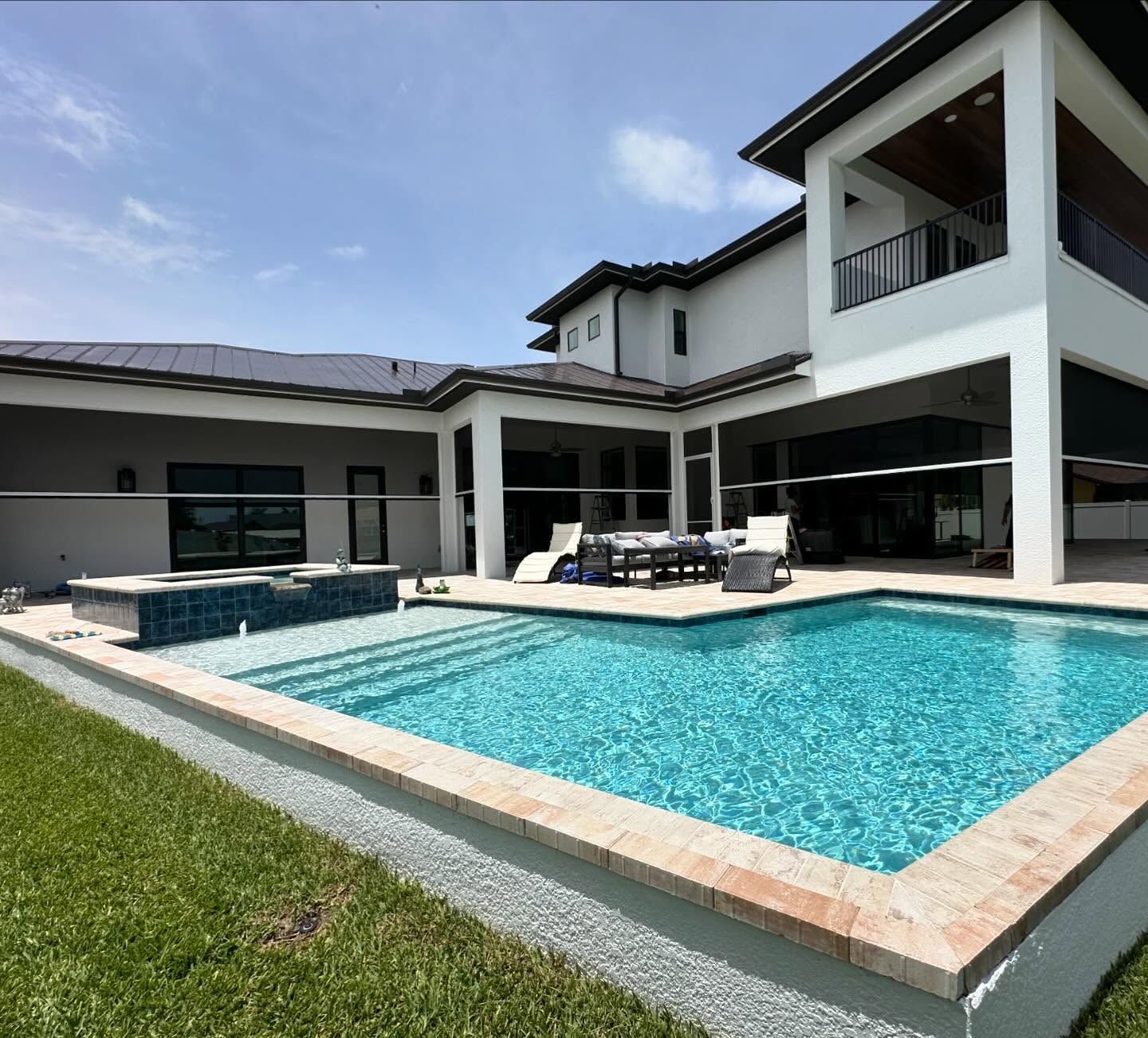 Modern white house with a turquoise swimming pool and patio seating under a blue sky