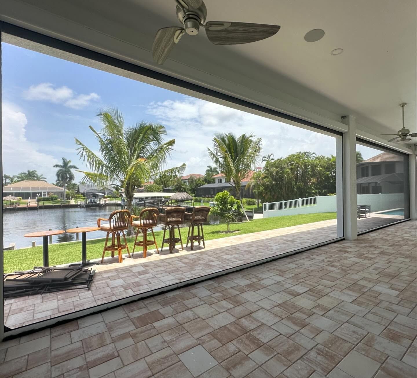 Covered patio with ceiling fans overlooking a palm-lined canal and outdoor dining area