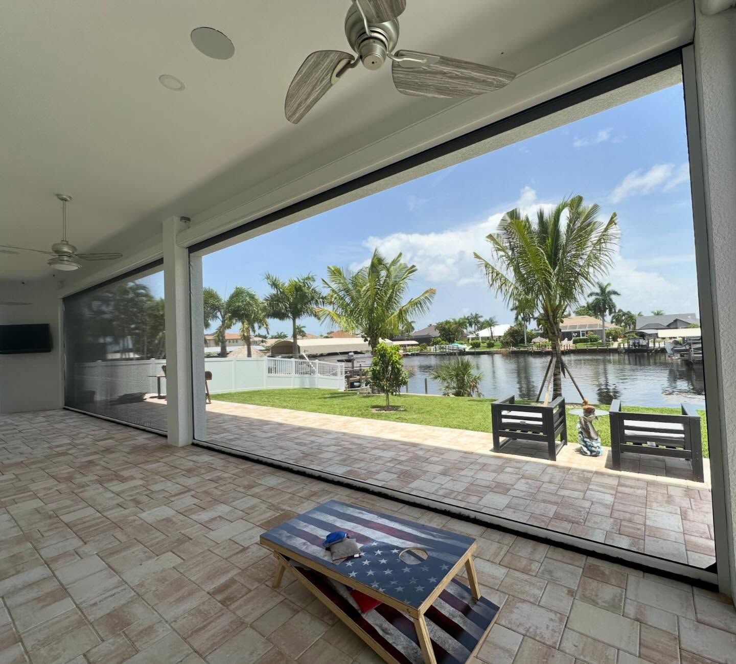 Covered patio overlooking a lake, with palm trees, tiled floor, and a small table in the foreground.