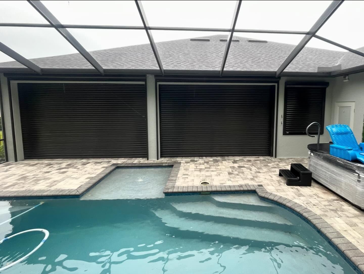Covered backyard pool with light blue water, stone deck, and closed gray shade screens.