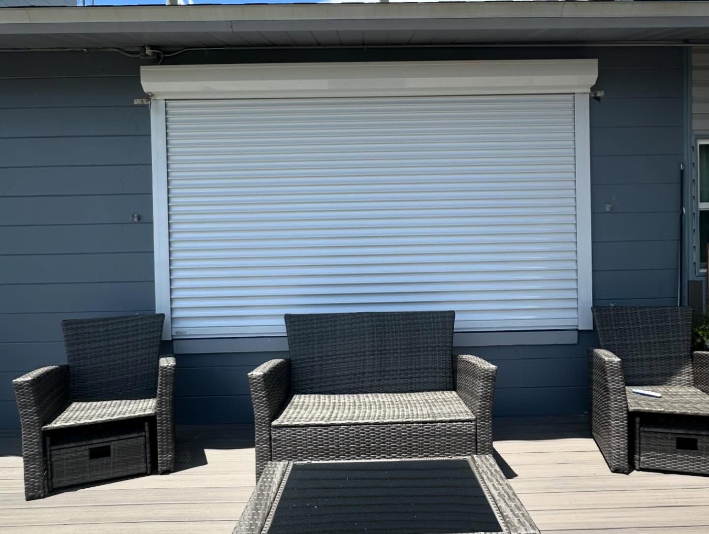 Outdoor patio with wicker chairs and a loveseat in front of a closed white window shutter