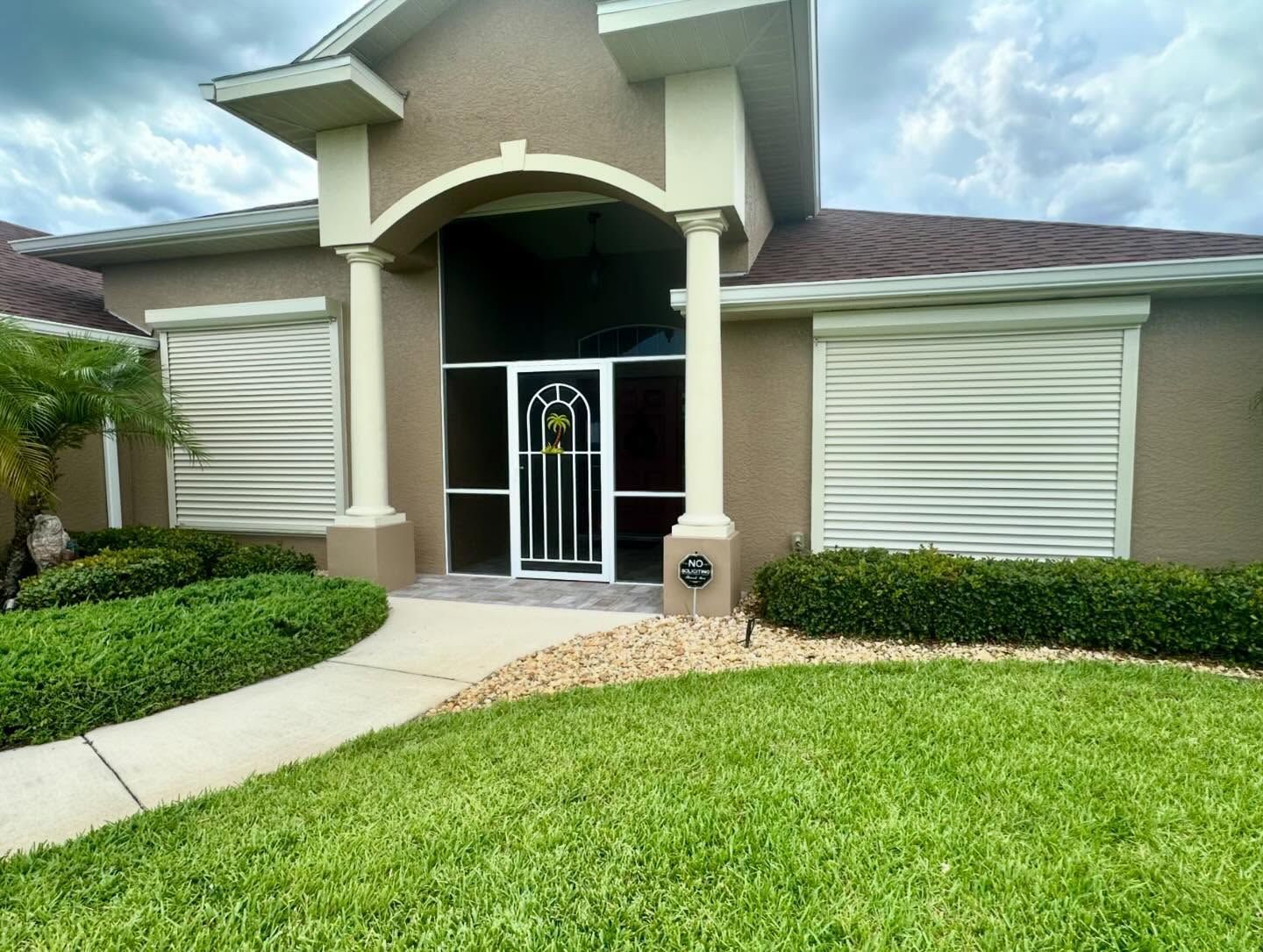 Front view of a beige house with a covered entry, white security gate, and green lawn