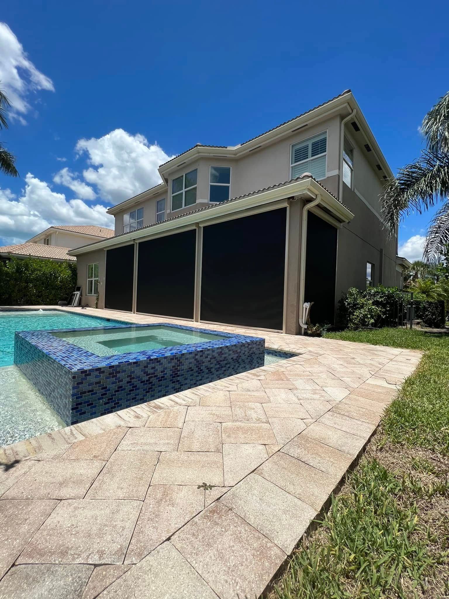 Backyard pool beside a two-story house with a covered patio and bright blue sky.