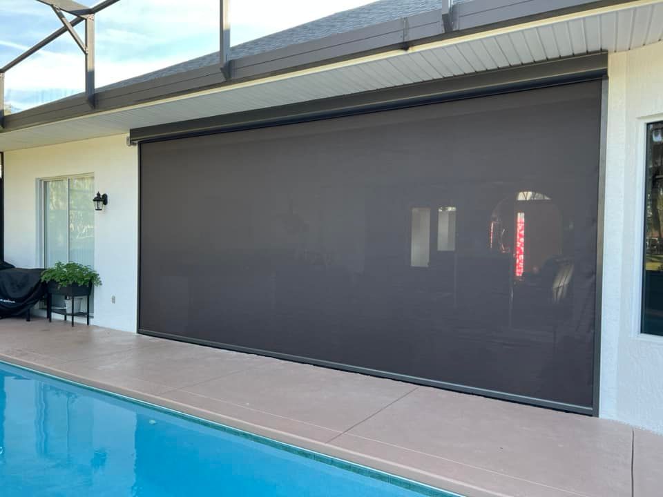 Outdoor patio with a large dark retractable screen beside a swimming pool