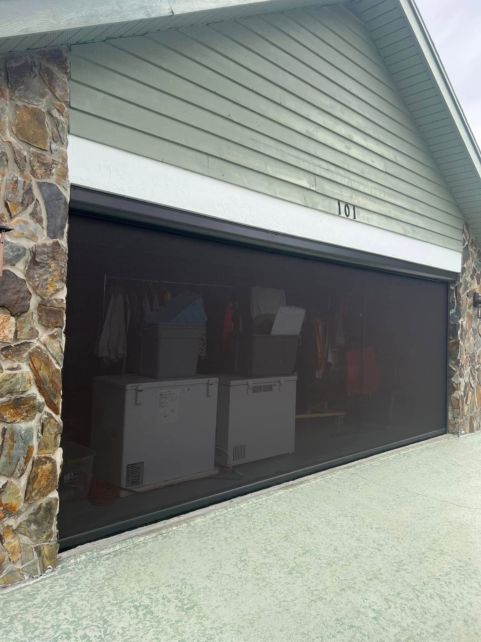 Open garage with dark interior and several white cabinets, framed by stone and gray siding.