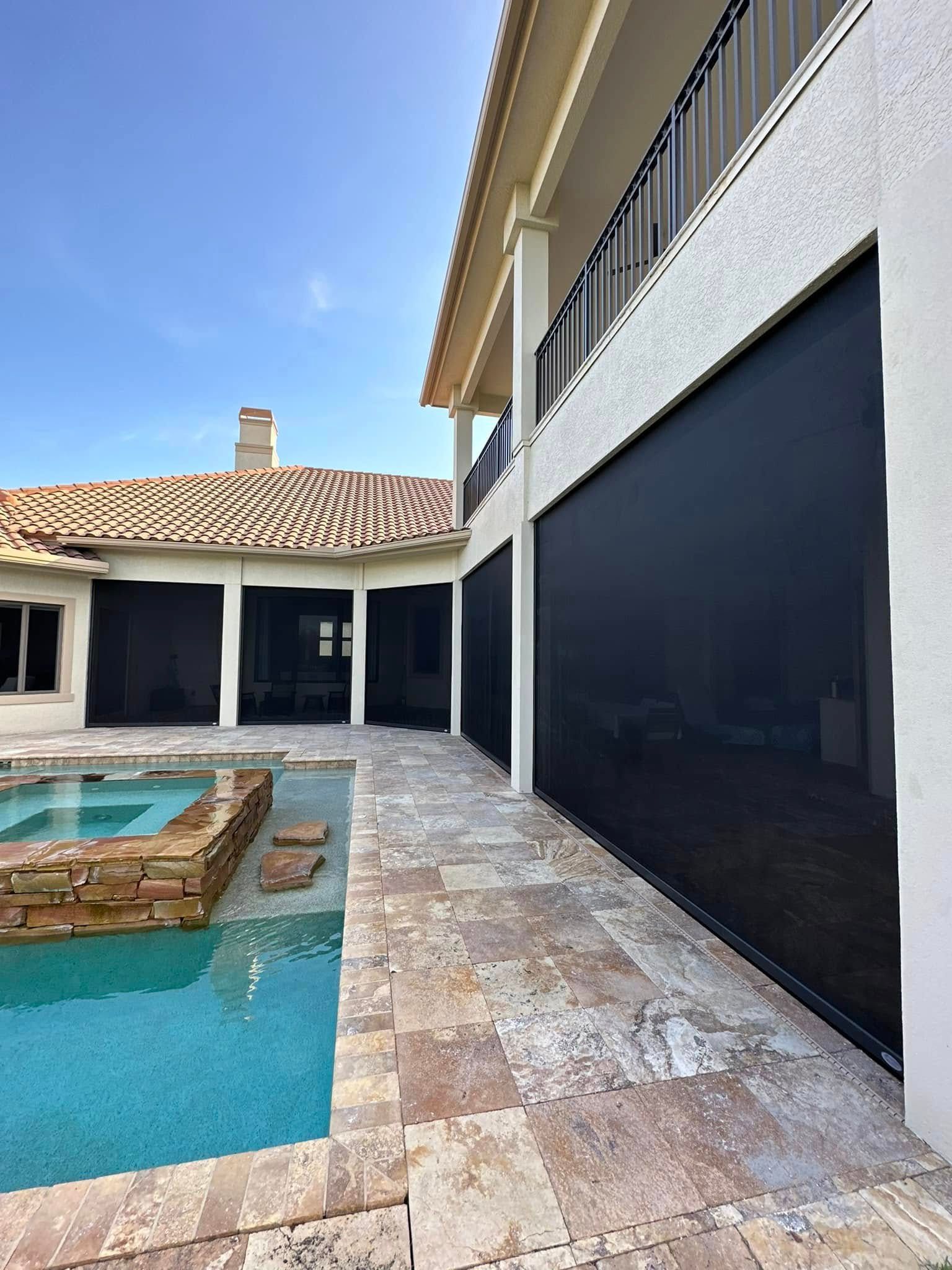 Backyard patio with pool, stone pavers, and white house walls under a clear blue sky