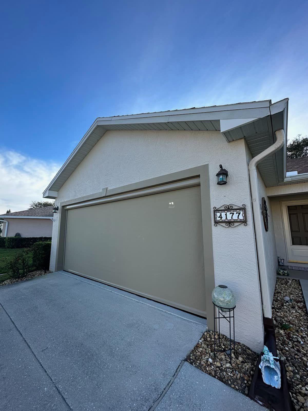 Suburban house exterior with a beige garage door, light stucco walls, and a blue sky overhead