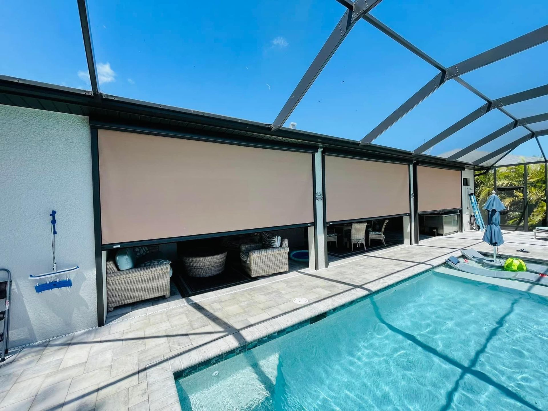 Covered outdoor pool with beige privacy shades and a person standing by the water