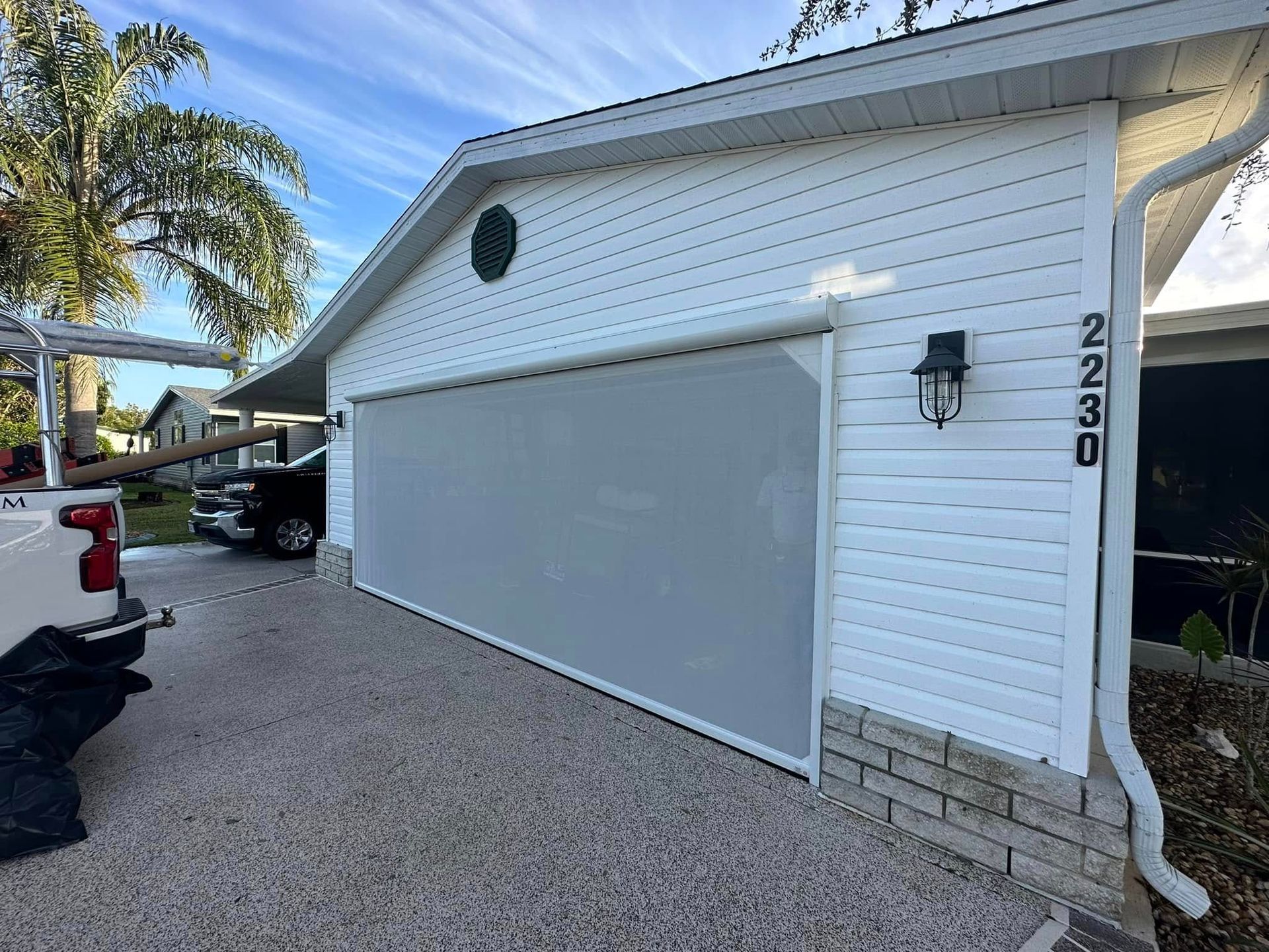 White garage with a closed gray door, house number 2230, and a pickup truck on a gravel driveway.