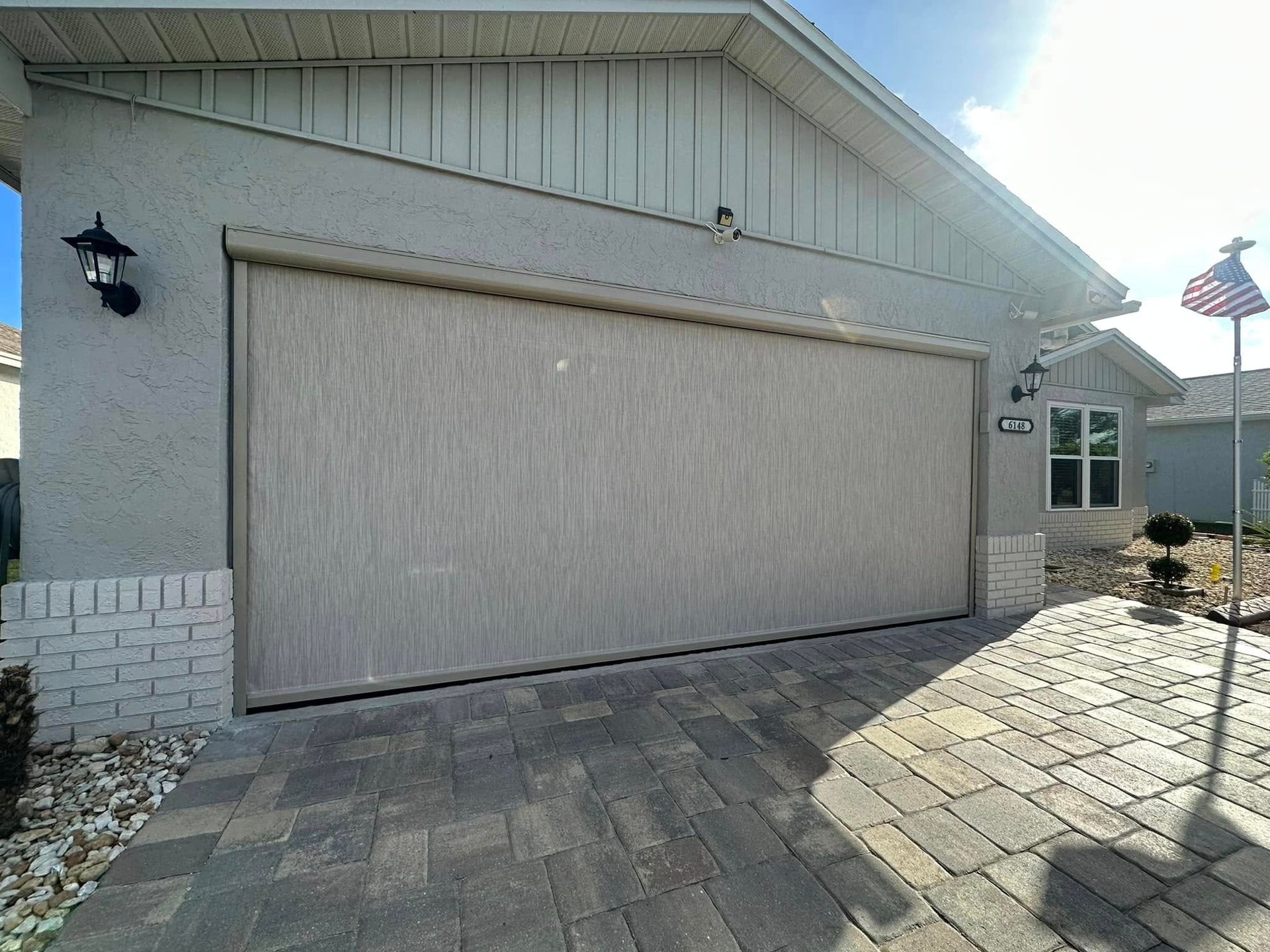 Closed beige garage door on a house with gray stucco exterior and stone driveway in bright sunlight