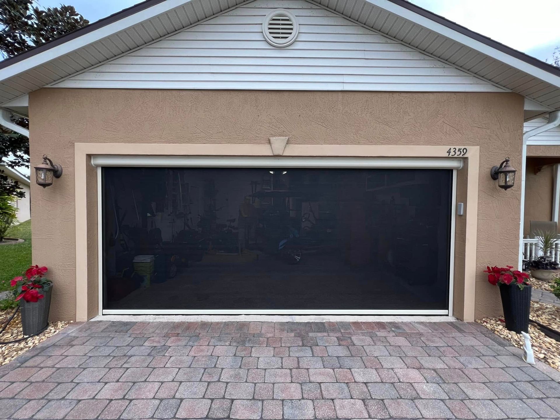 House front with a wide two-car garage door, brick driveway, and potted plants on both sides