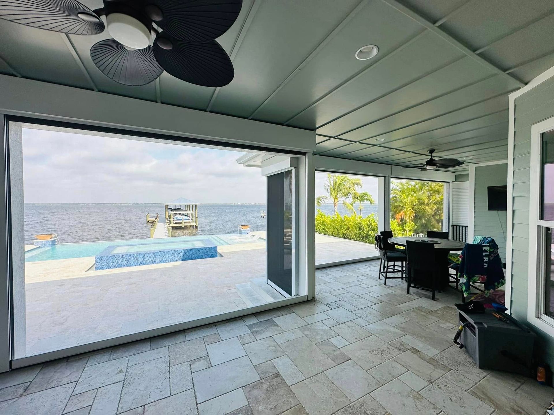 Covered patio with open view of a pool and ocean, featuring tiled floor, ceiling fans, and outdoor seating.