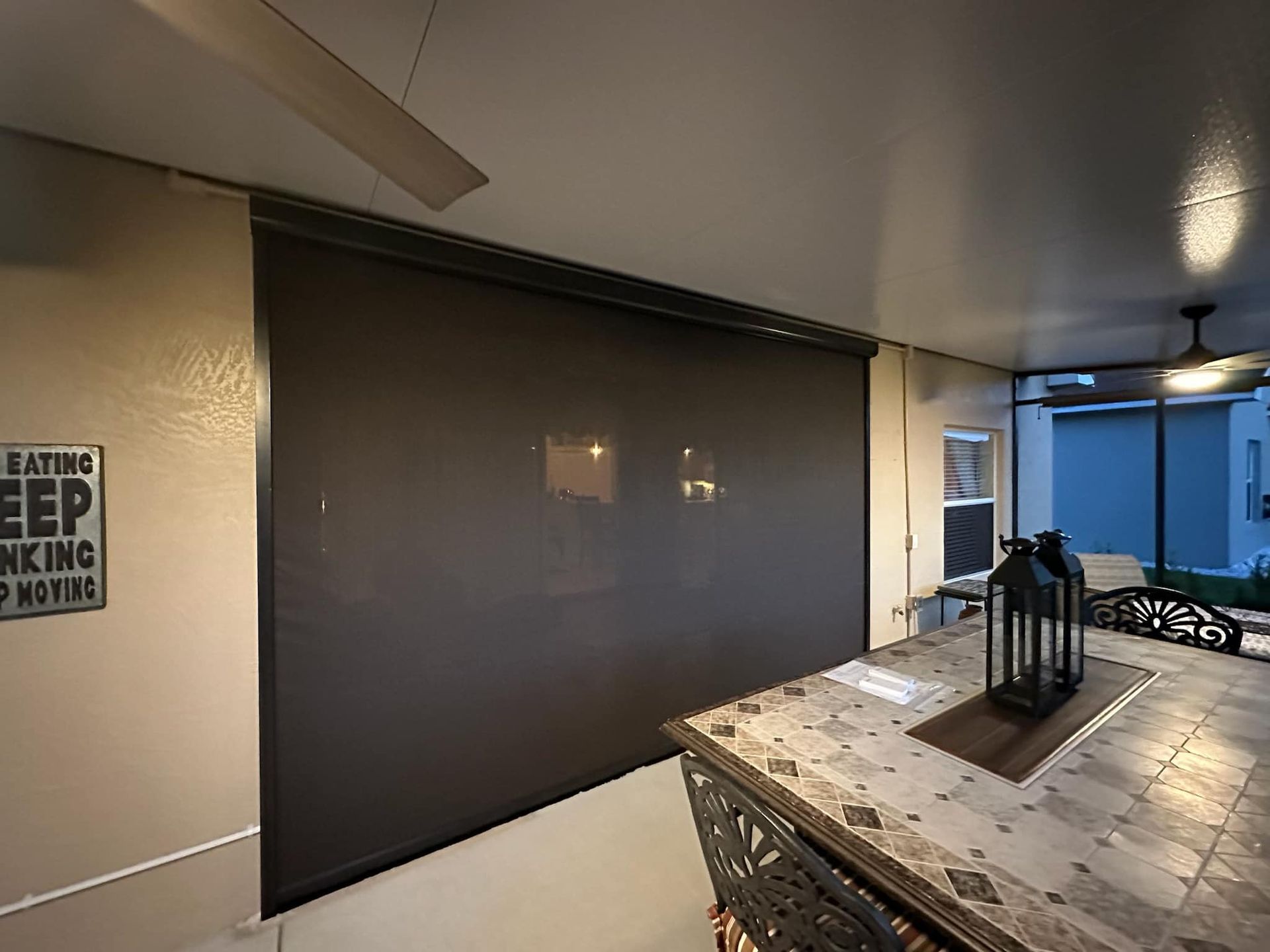Covered patio with a dark retractable shade, tiled table, and a small sign on the wall.