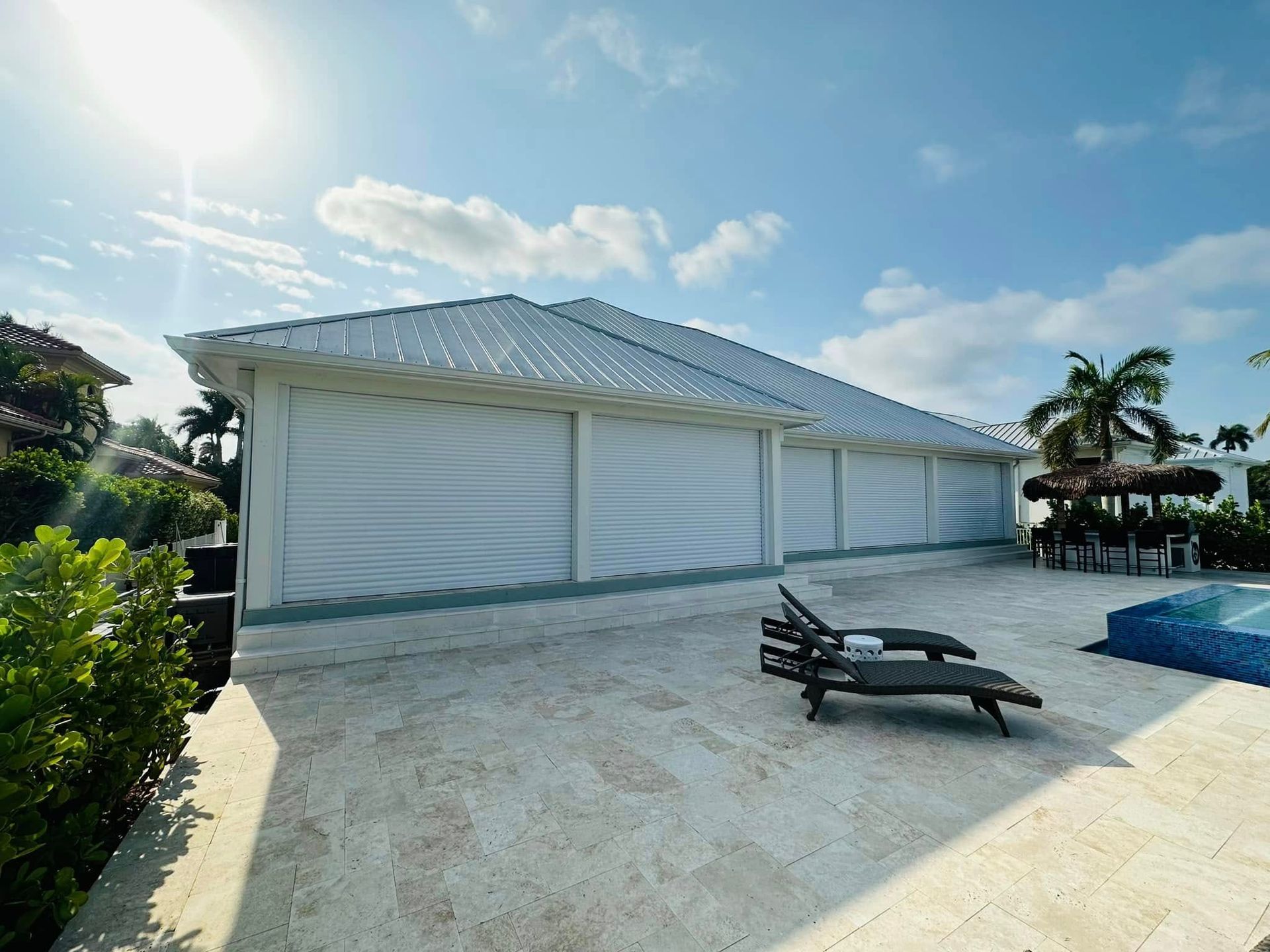 White beach pavilion with lounge chairs on sandy ground under a bright blue sky, beside a pool