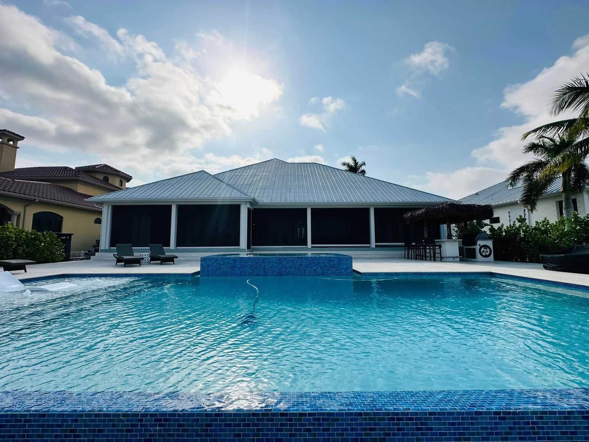 Luxury backyard pool with blue water, patio, and a modern house under a bright sky