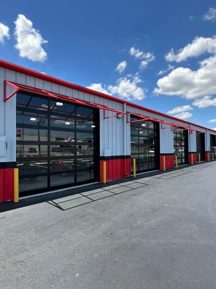 Modern industrial building with red trim and large glass garage doors under a blue sky