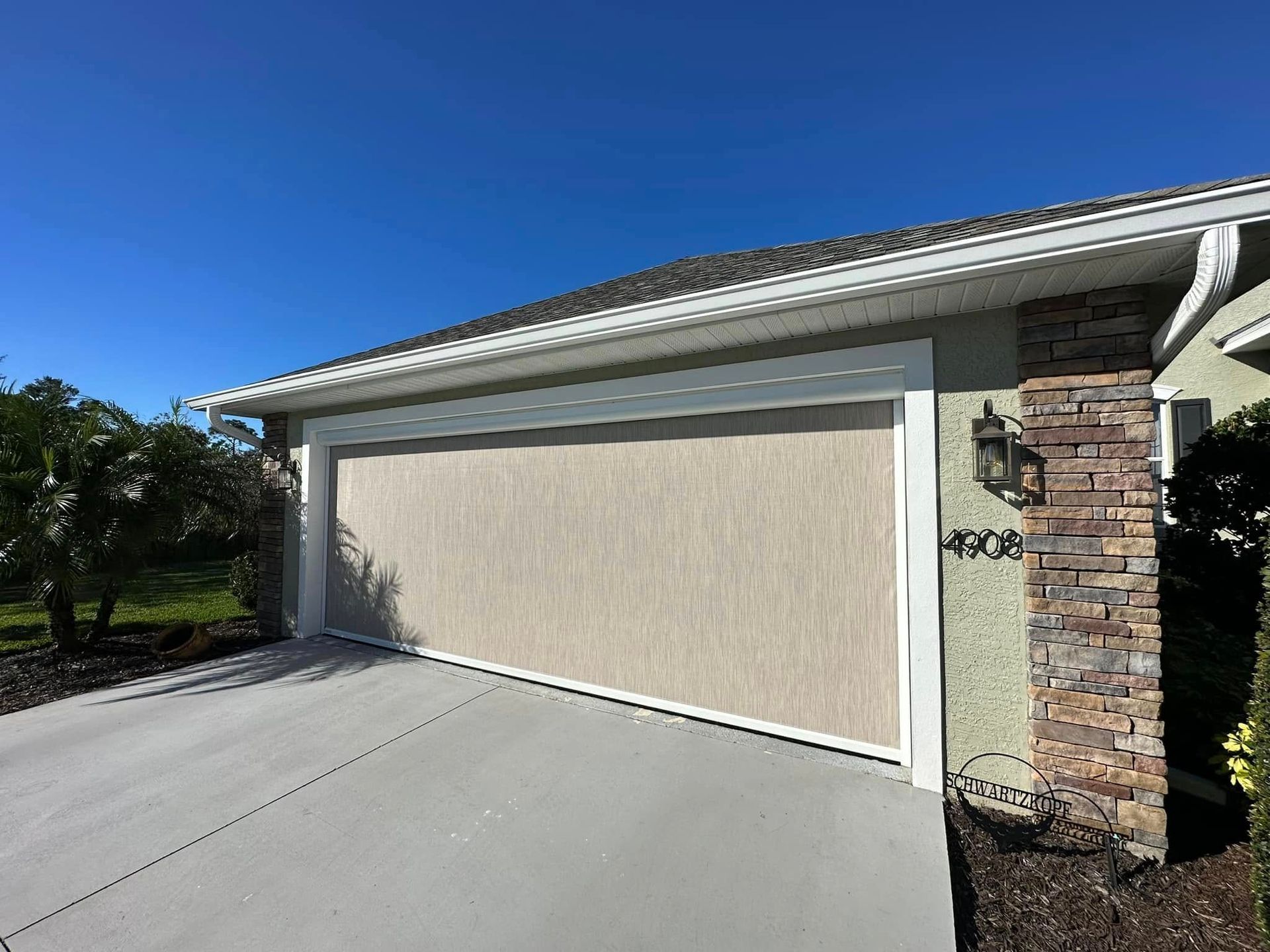 Closed beige garage door on a suburban house with a brick column and concrete driveway.