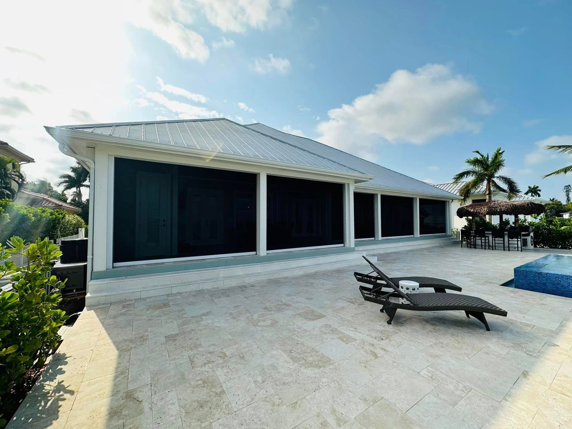 Modern white villa with a large tiled patio, lounge chairs, and a pool under a bright blue sky