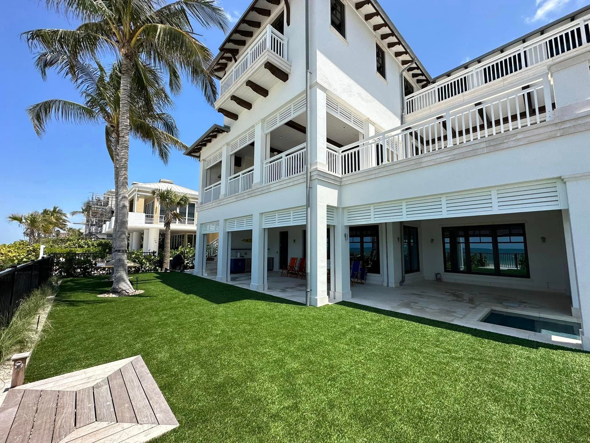 White beachfront house with balconies, palm trees, and a green lawn under a bright blue sky