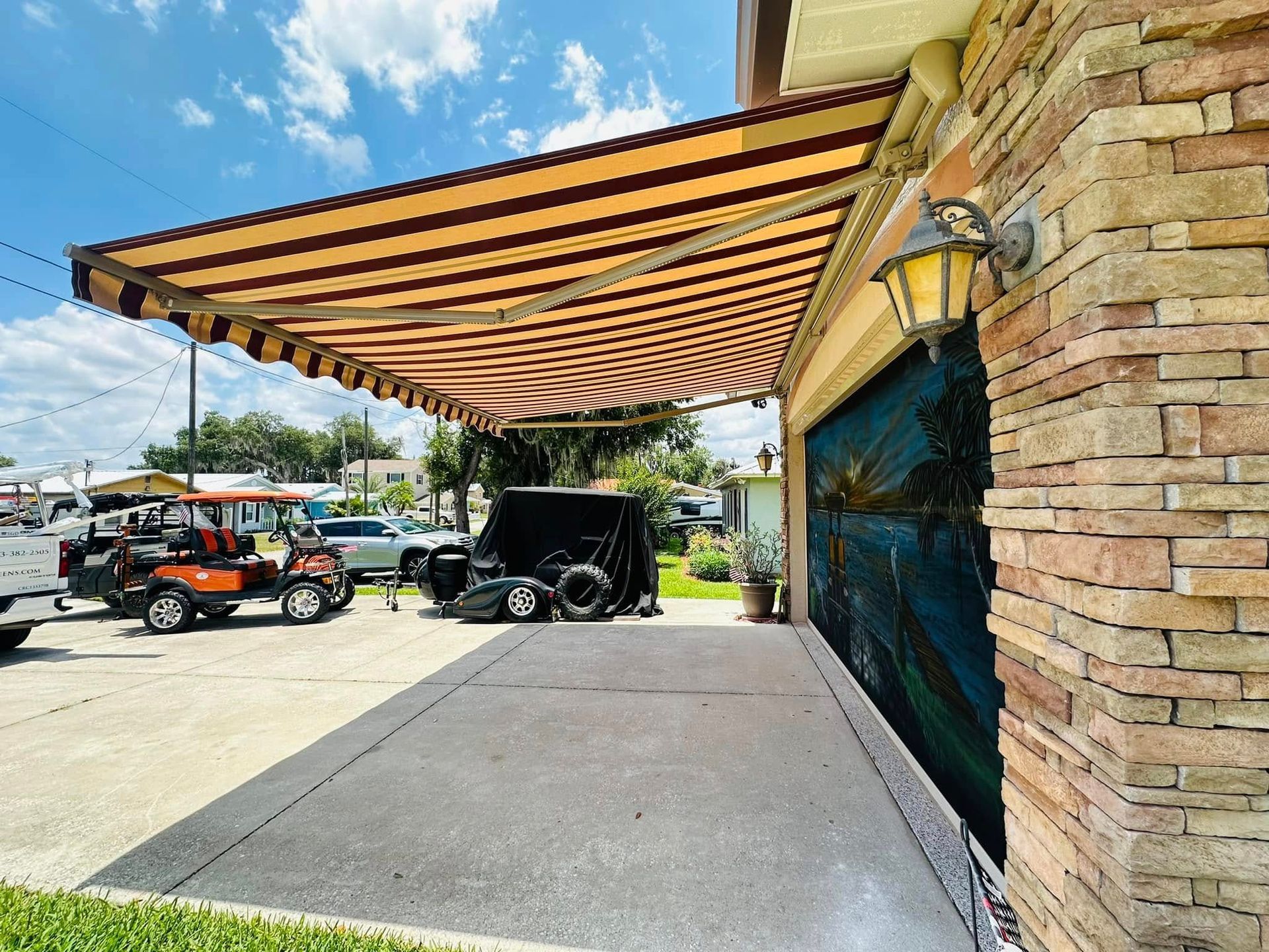 Outdoor patio with tan striped awning, stone wall, and parked off-road vehicles under a sunny blue sky