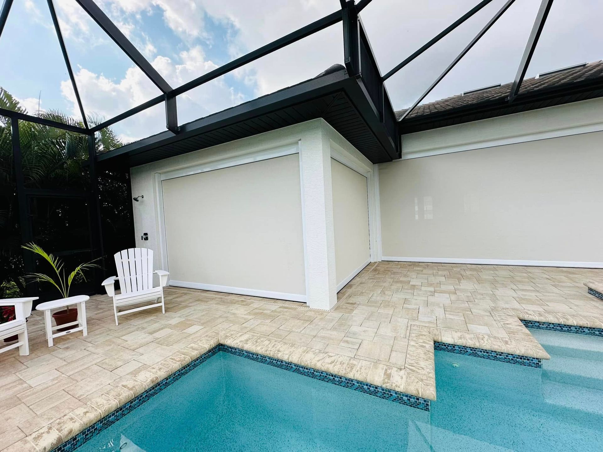 Poolside patio with white chairs, beige pavers, and screened enclosure around a turquoise pool
