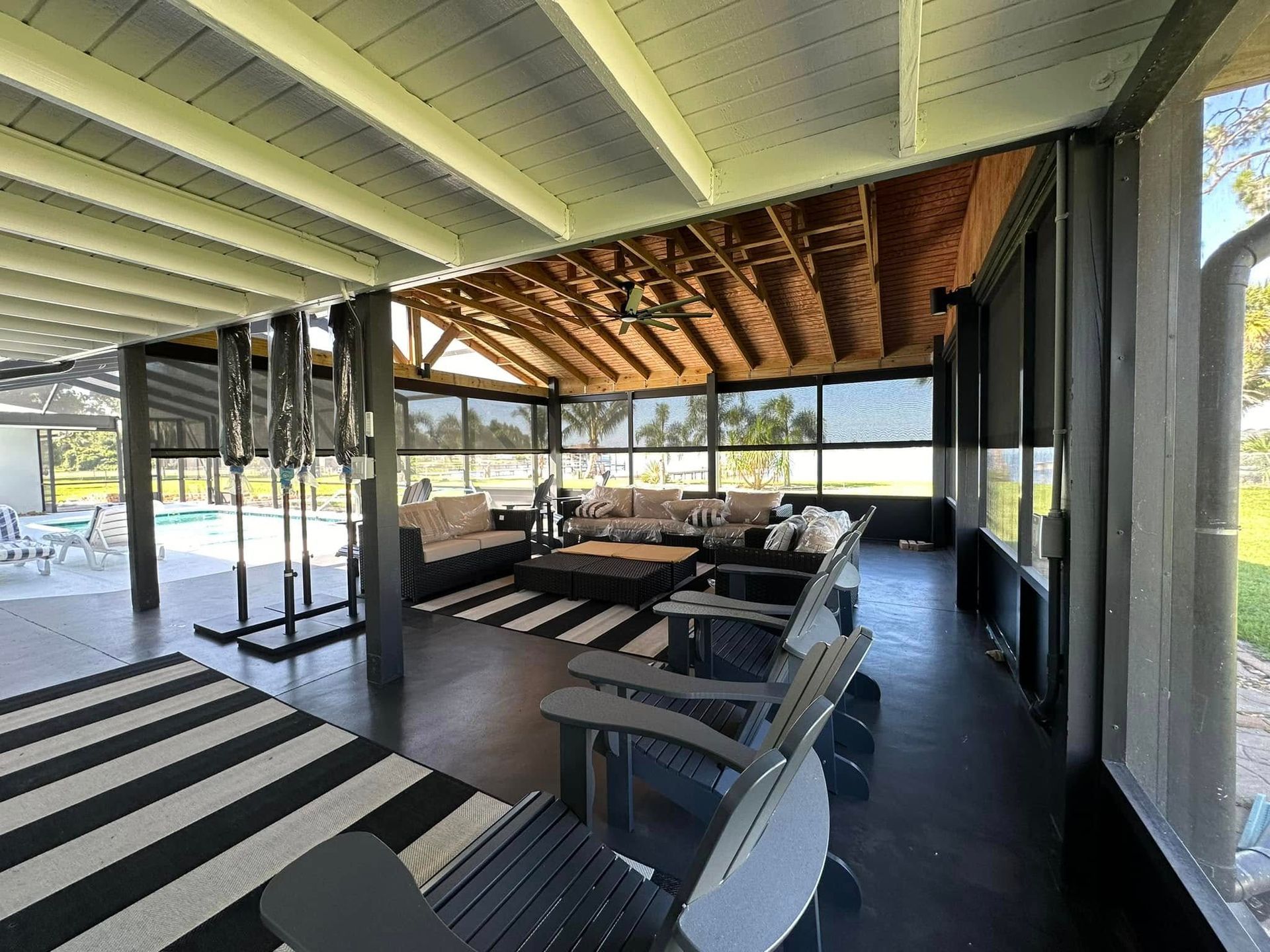 Covered outdoor lounge with tables and chairs, striped rug, and open view to the pool area.